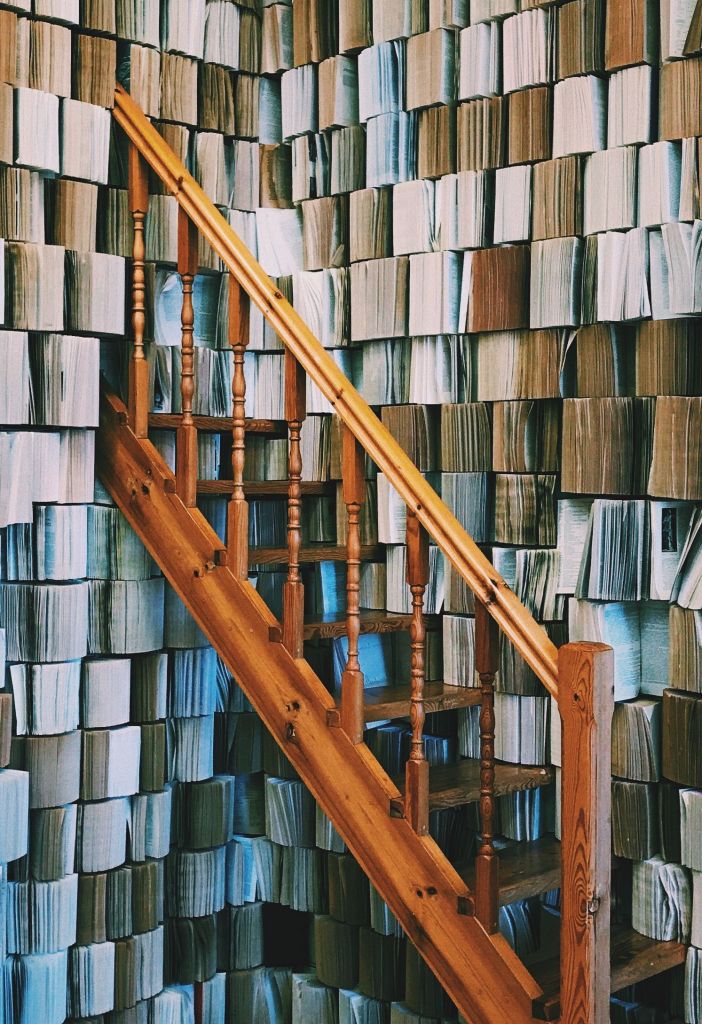 Brown wooden staircase disappearing into a wall made of books
